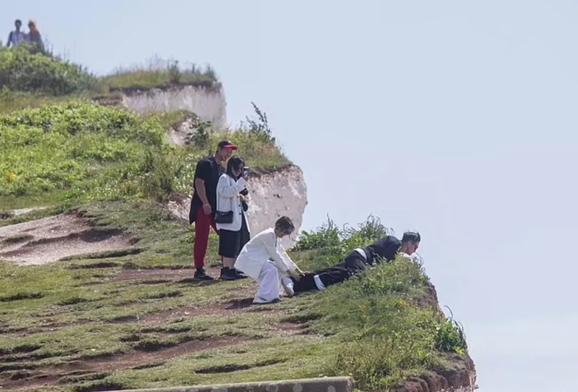 туристи на краю скелі тримають ще одного за ноги