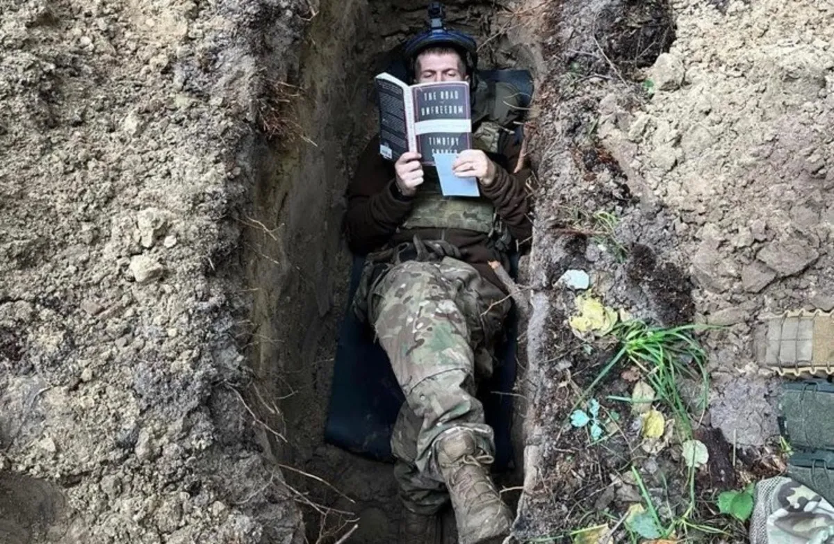 Воин читает книгу Снайдера в окопе