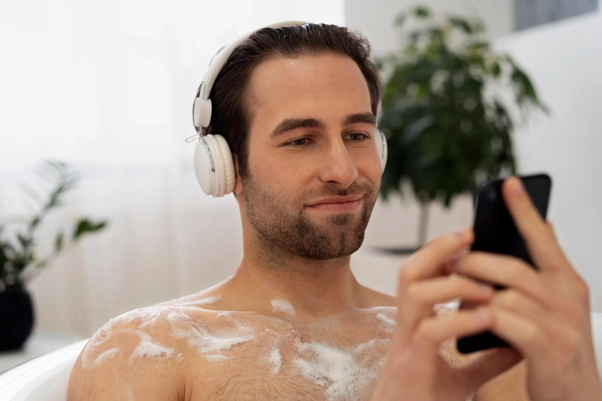 Мужчина принимает ванну и читает что-то в смартфоне