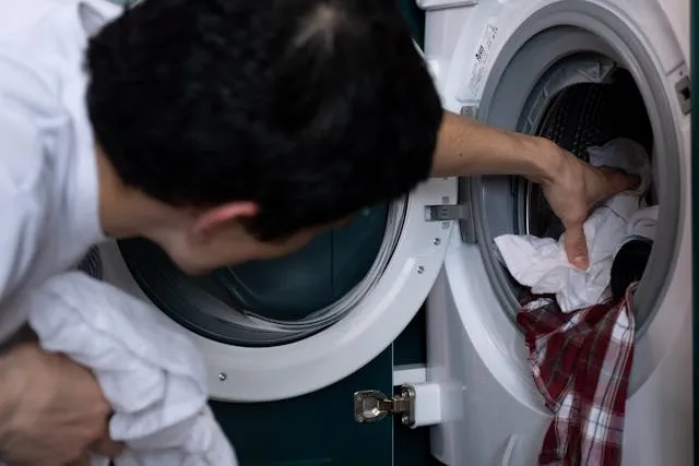 Мужчина кладет грязную одежду в стиральную машинку