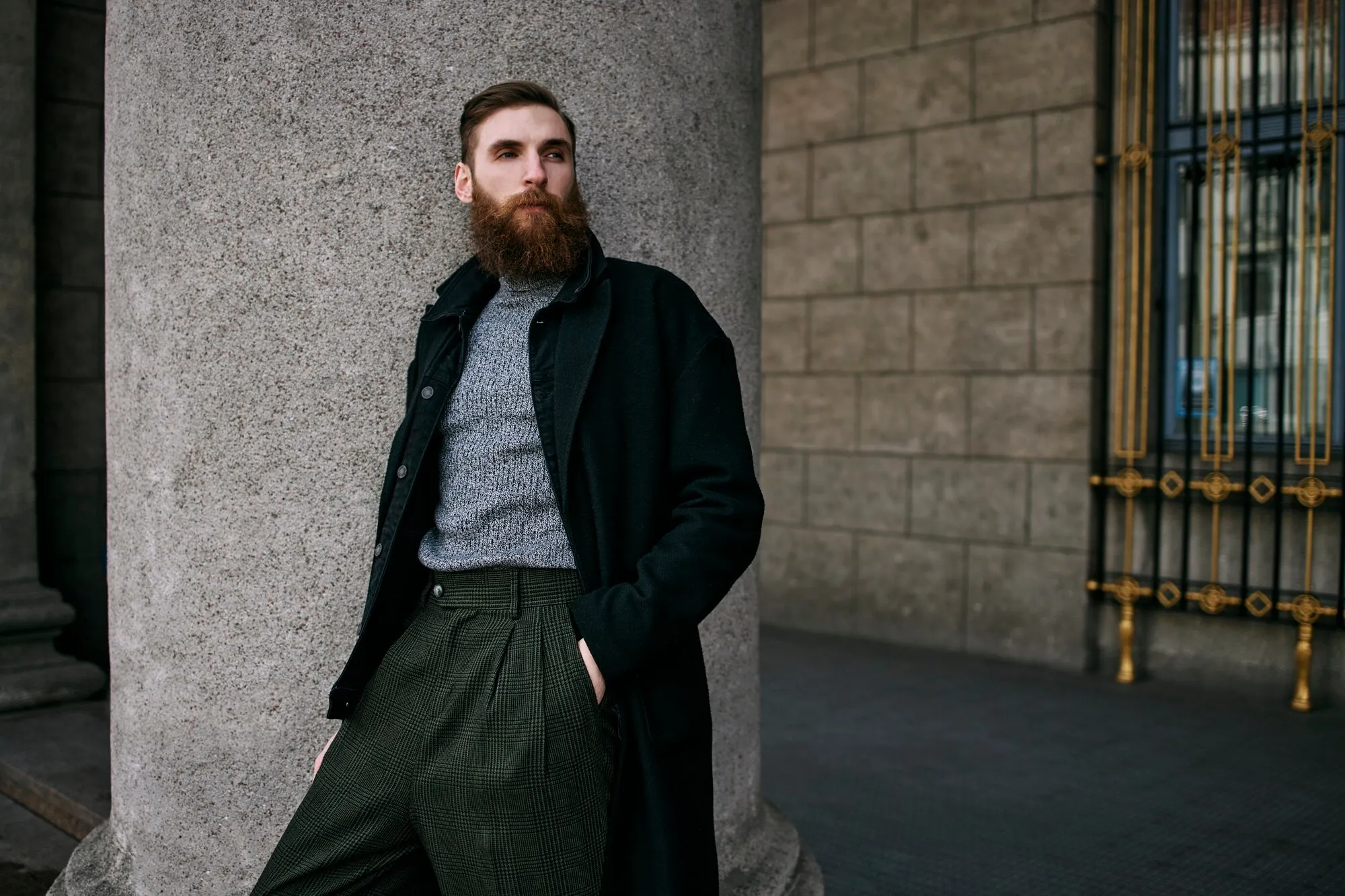 Бородатий чоловік у пальто та штанах стоїть на вулиці