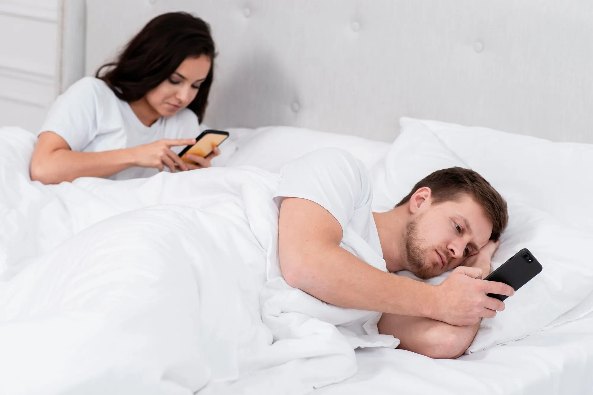 Мужчина и женщина смотрят что-то в смартфонах в постели